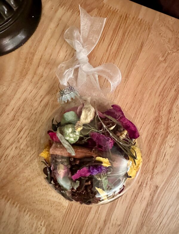 colorful dried flowers and herbs in a glass disc shaped ornament against a wood background