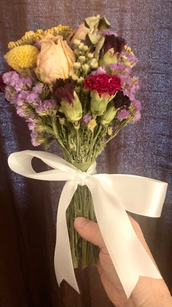 colorful dried flower bouquet of roses carnations statice yarrow and craspedia flowers tied with a white satin ribbon on a brown background
