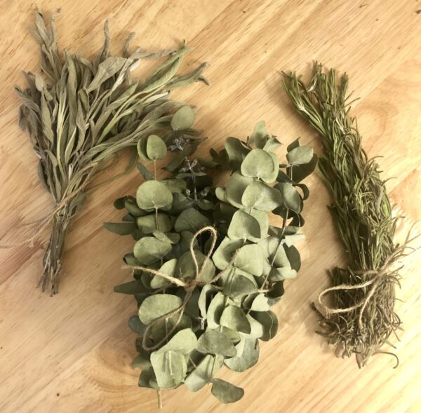 dried bundles of sage, eucalyptus, and rosemary herbs on a wood background