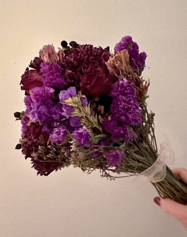 a hand holding a purple dried flower bouquet