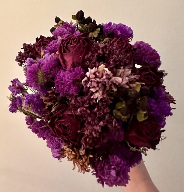 a hand holding a purple dried flower bouquet