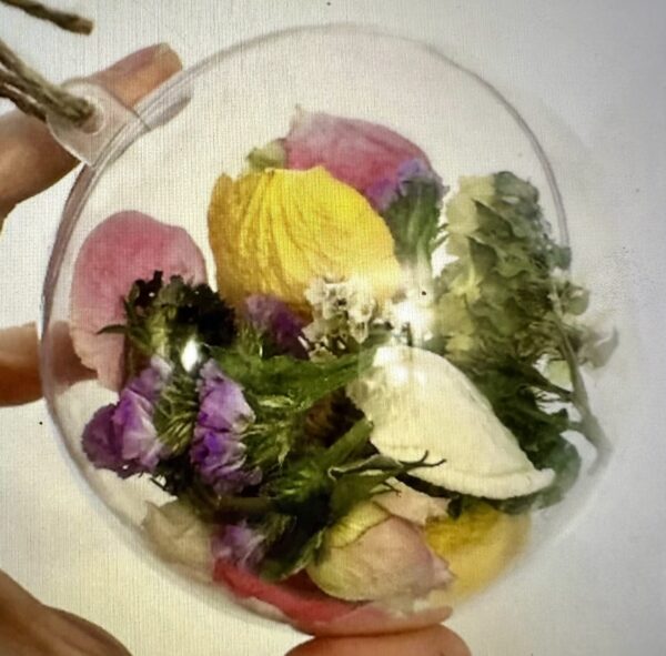 a hand holding a ball ornament with dried flowers and rose petals
