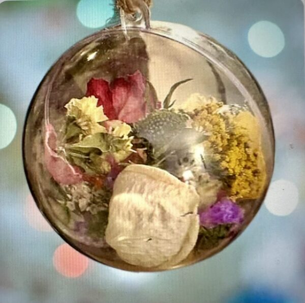 Rose petals and flower heads in a shatterproof ball ornament against a festive light background