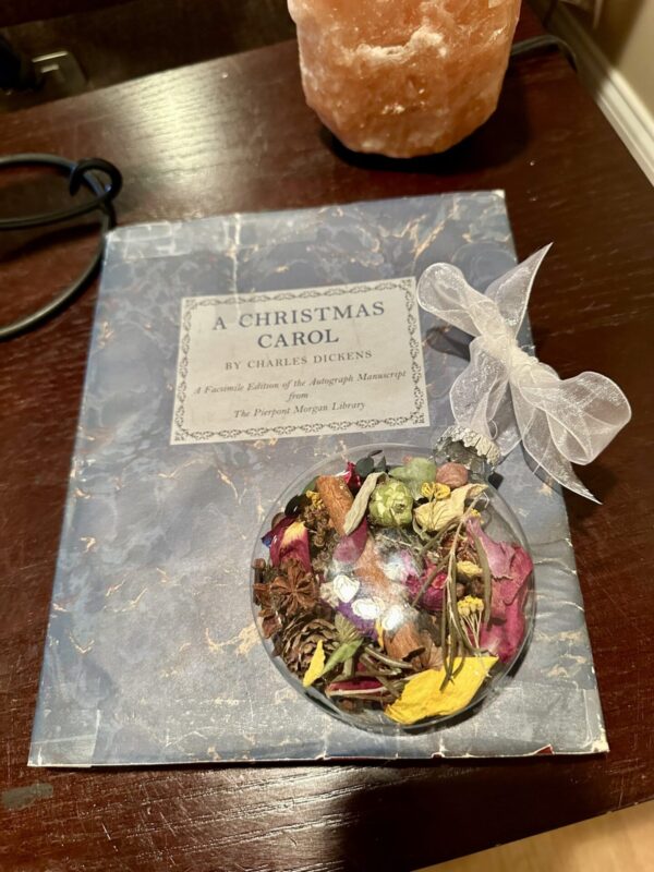 disc shaped ornament with dried herbs and flowers sitting on a blue charles dickens Christmas Carol book on a brown table